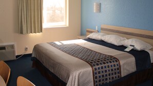 A hotel room with a bed, a window with curtains, a wall-mounted light, and a thermostat.