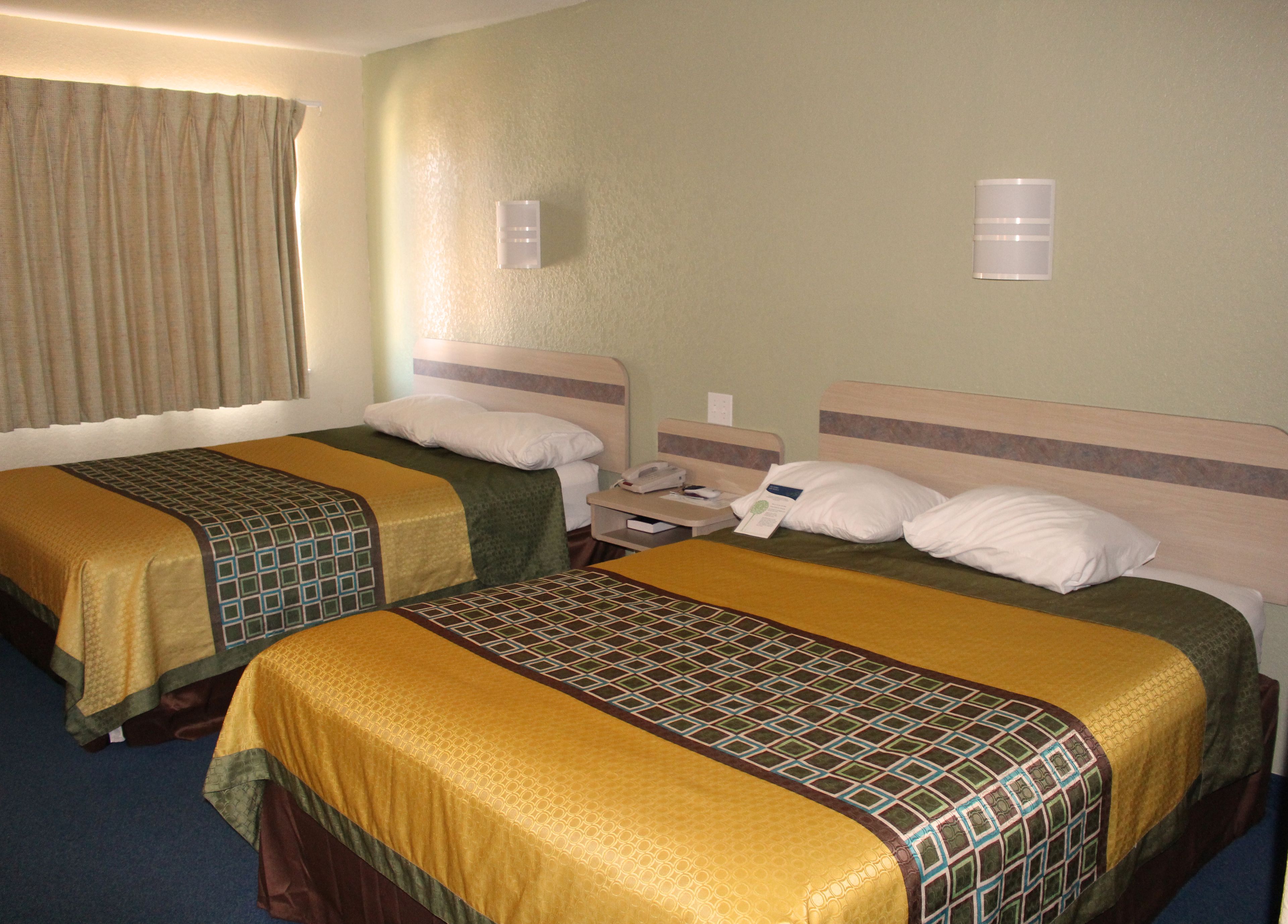 A hotel room with two beds, each with a patterned bedspread, a bedside table with a phone, and a wall-mounted light.