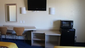 A hotel room with a TV, a microwave, a desk, two chairs, and a bed.