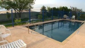 A swimming pool with a blue border, surrounded by a fence and a few chairs.