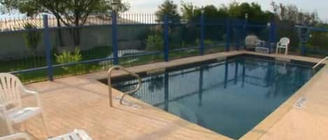 Piscina con bordo blu, circondata da una recinzione e qualche sedia.