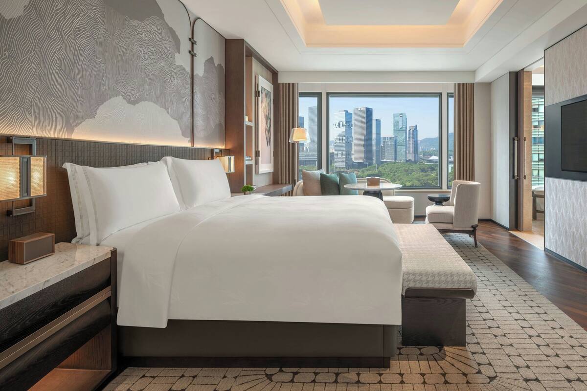 Una habitación de hotel moderna con una cama grande, vistas a la ciudad, un escritorio y una zona de estar acogedora.