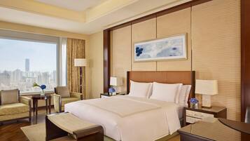 A hotel room with a large bed, two armchairs, a desk, and a view of the city.