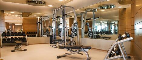 A gym with weightlifting equipment, mirrors, and a wooden floor.
