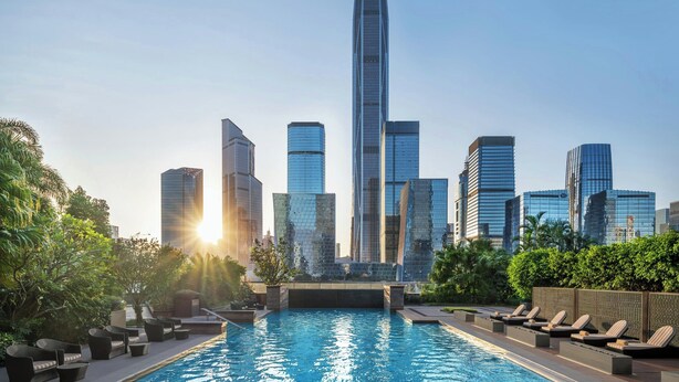 Una piscina en la azotea con sillones de descanso, rodeada de vegetación, y un horizonte urbano con modernos rascacielos al fondo.