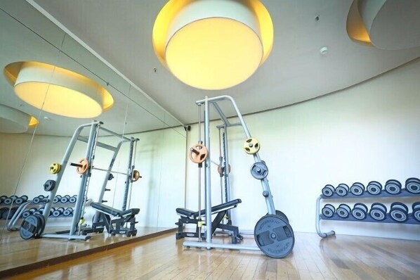 Un gimnasio con equipo de levantamiento de pesas, una banca y un estante con mancuernas.
