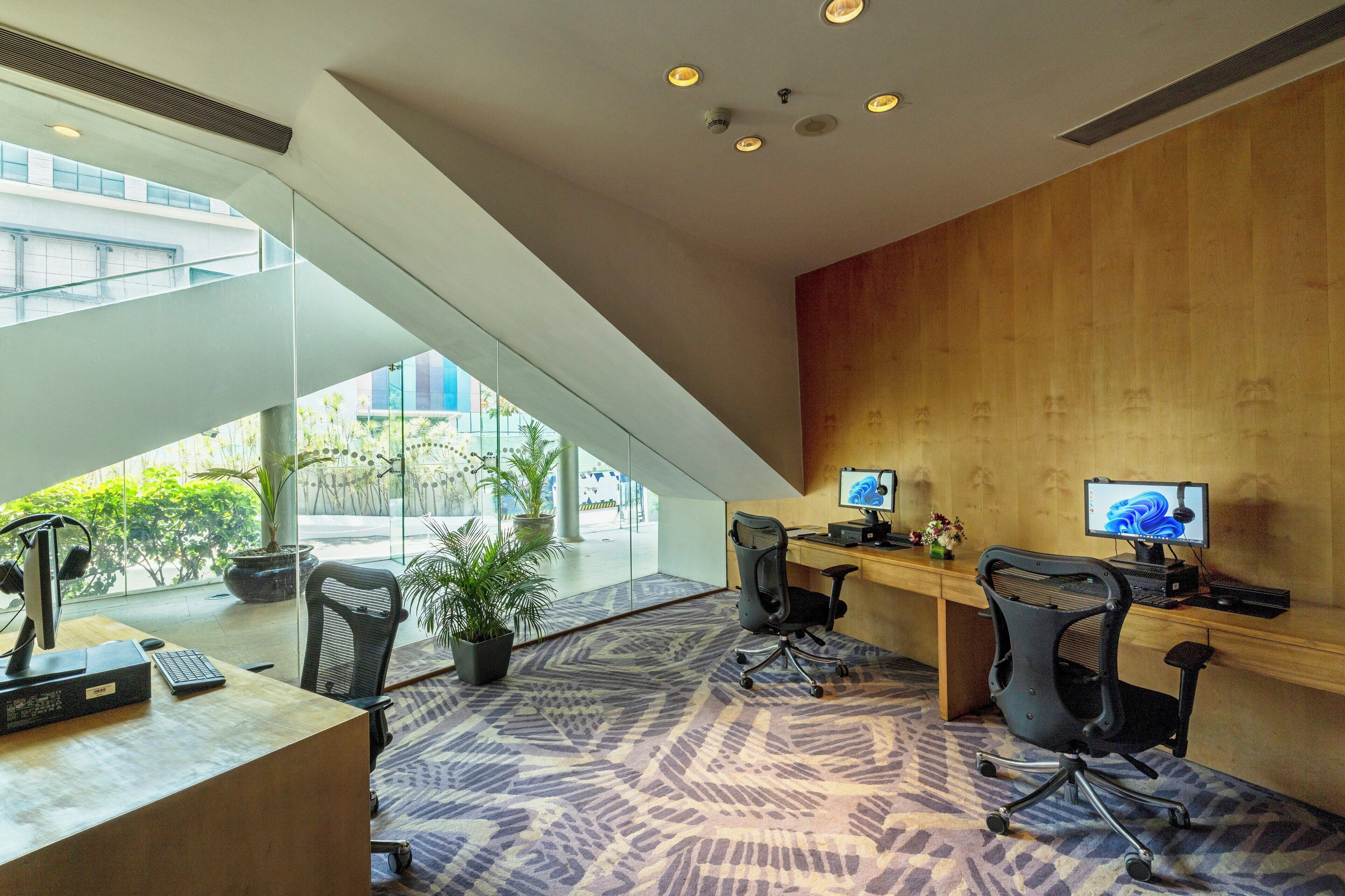 Un espacio de oficina moderno con paredes de vidrio, un escritorio de madera, dos monitores y sillas ergonómicas.