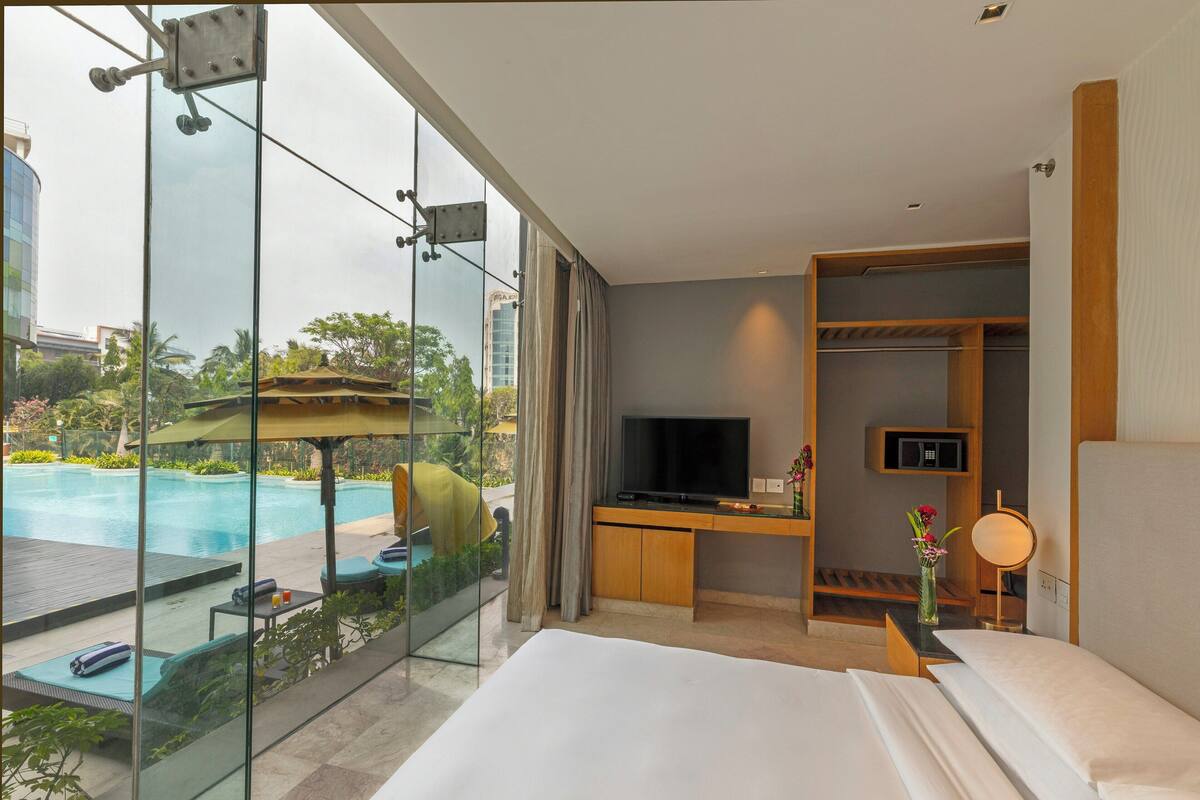 A hotel room with a large bed, a TV, a desk, and a view of a swimming pool.