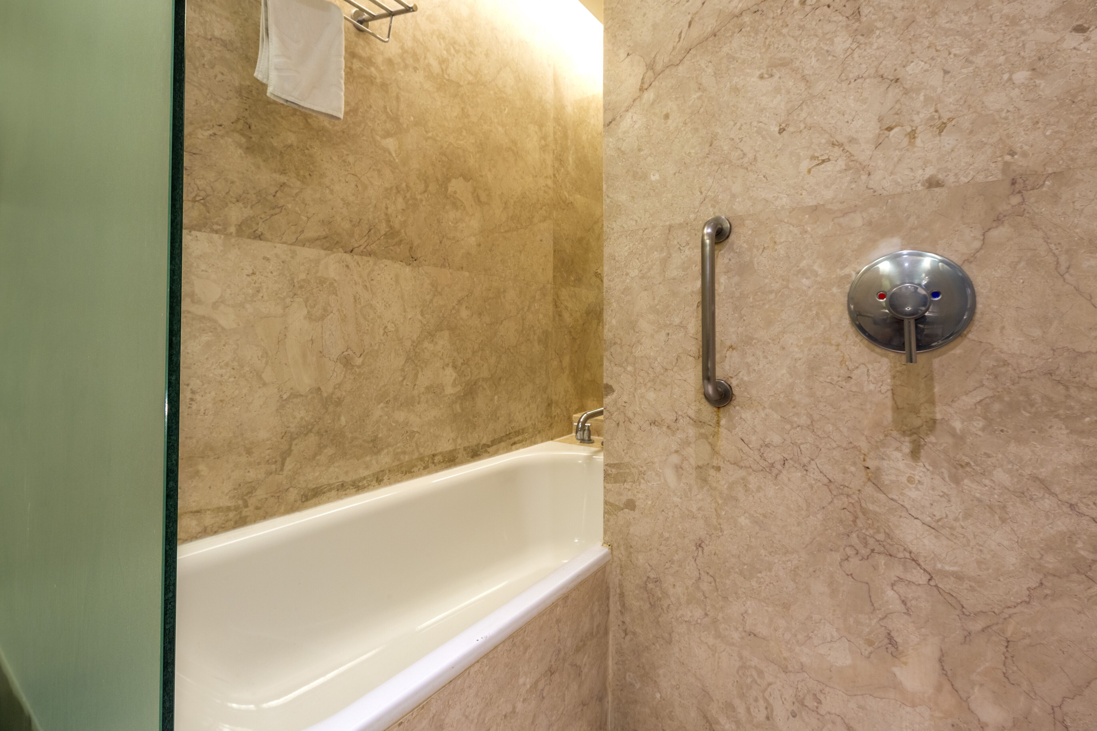A bathroom with a white bathtub, a handrail, and a marble wall.