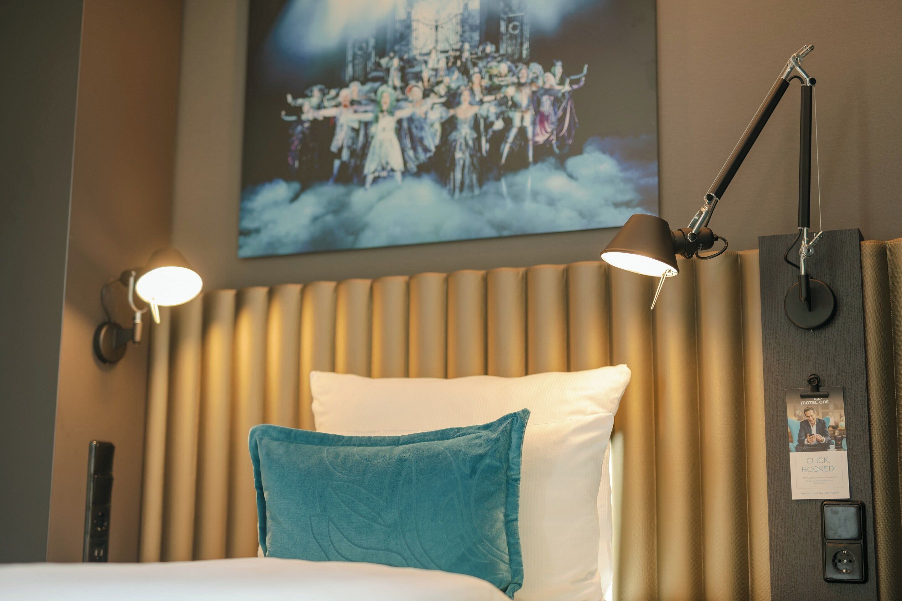 Une chambre d’hôtel avec un lit, une tête de lit, une lampe fixée au mur et un tableau.