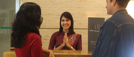A reception desk with a woman standing behind it, a man and a woman facing her.