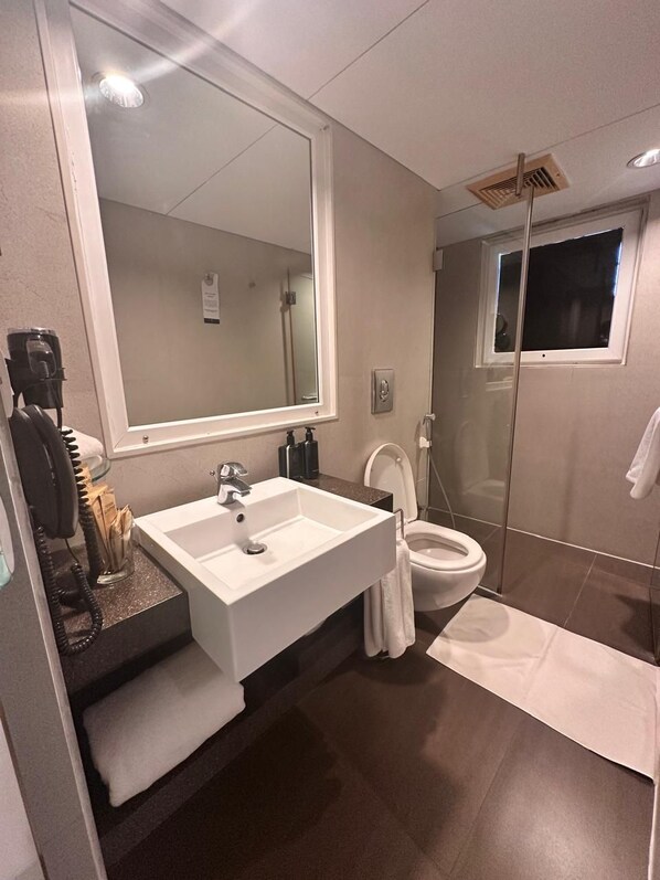 A modern bathroom with a large mirror, a sink, a toilet, and a shower.