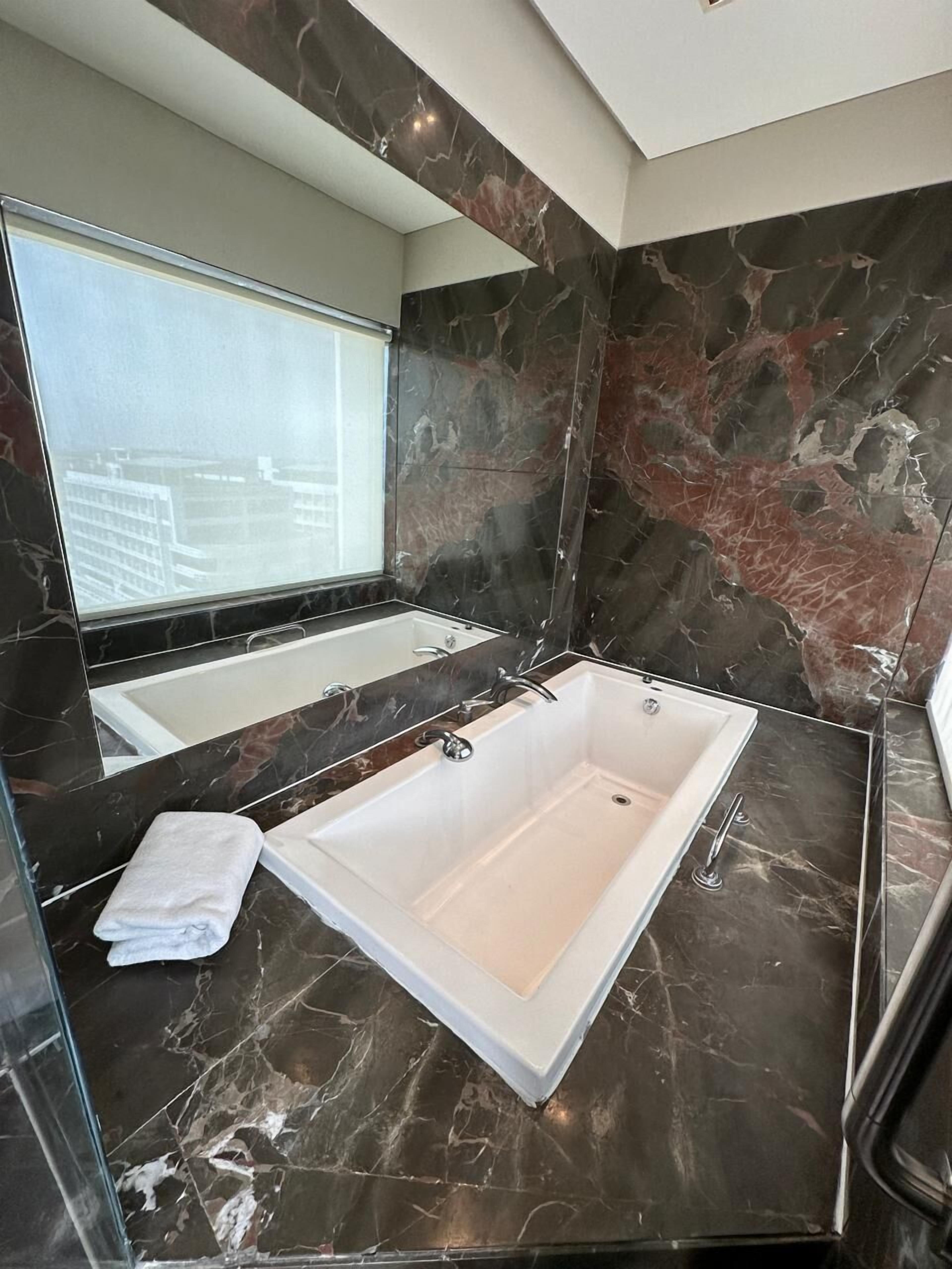 Une salle de bain moderne avec une grande baignoire, un miroir et une fenêtre.