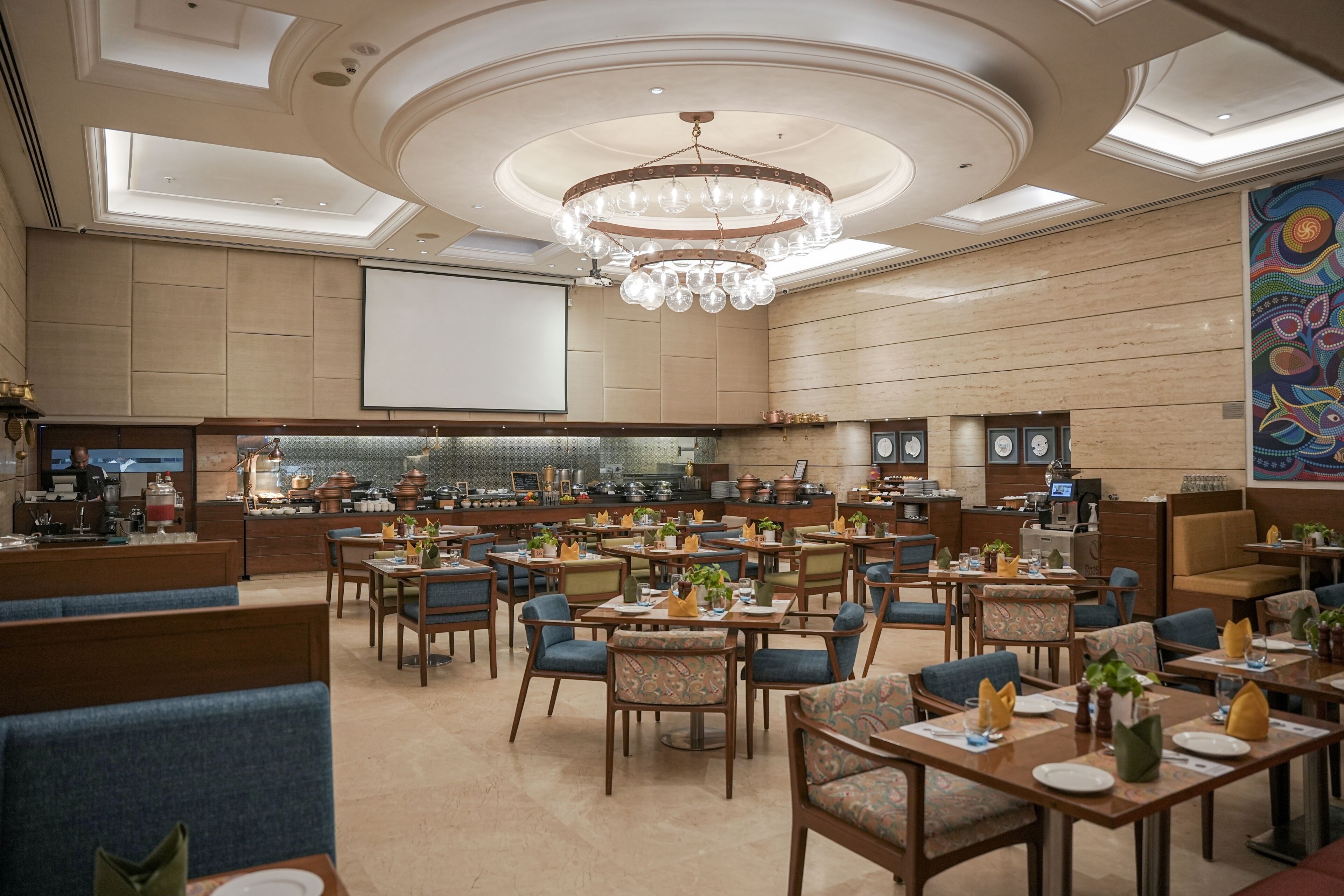 A spacious hotel lobby with a central bar, multiple seating areas, and a large chandelier.