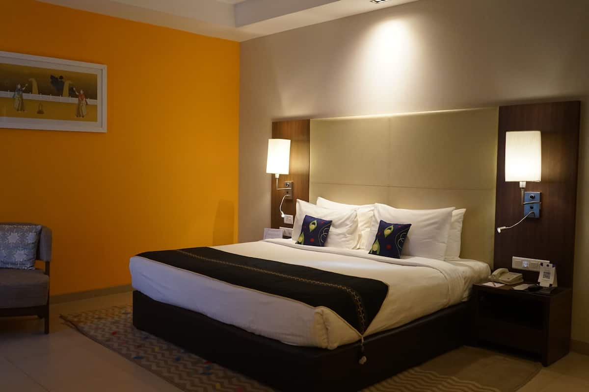 A hotel room with a bed, bedside tables, a chair, and a painting on the wall.