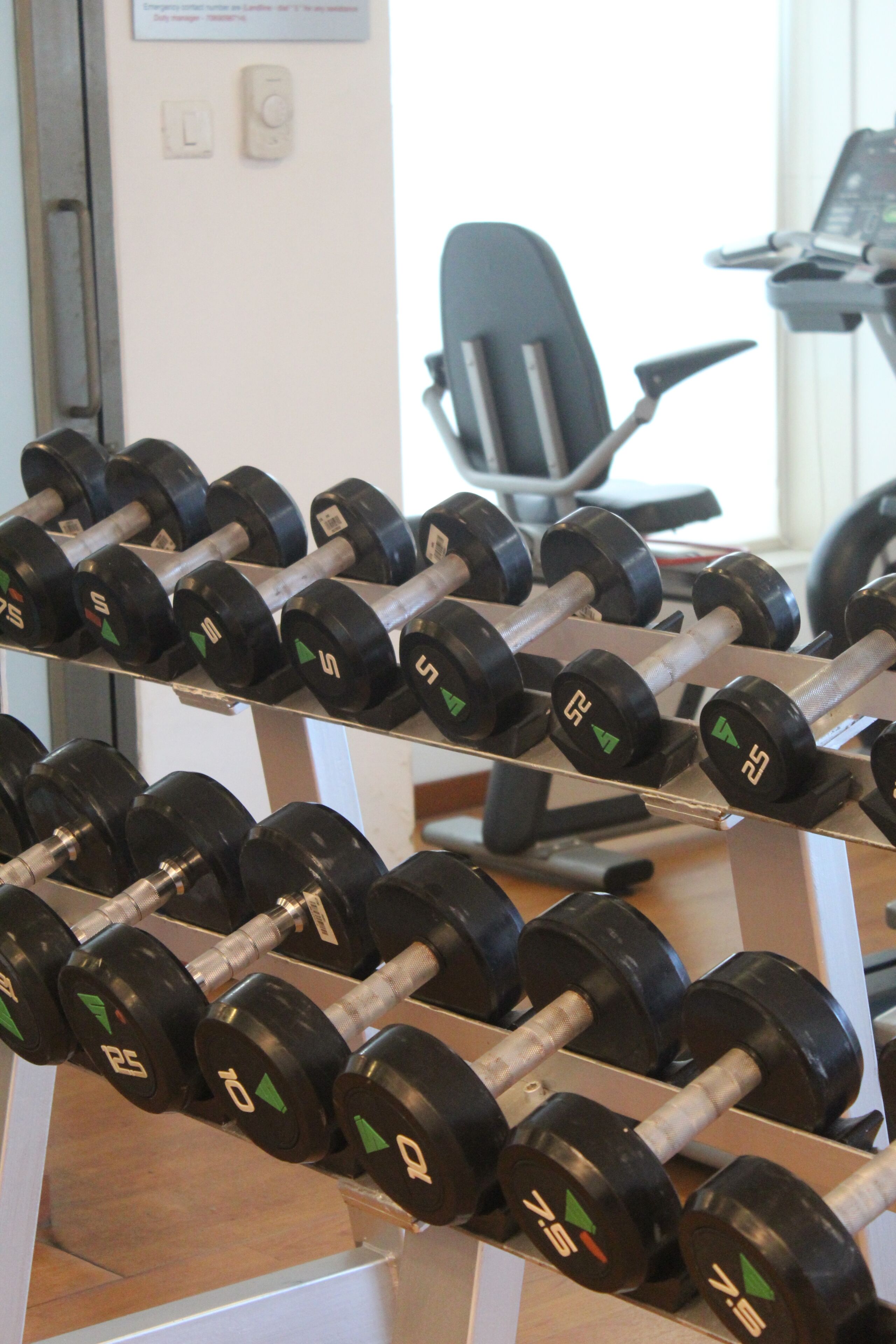 A row of black dumbbells with green and red markings on a rack.