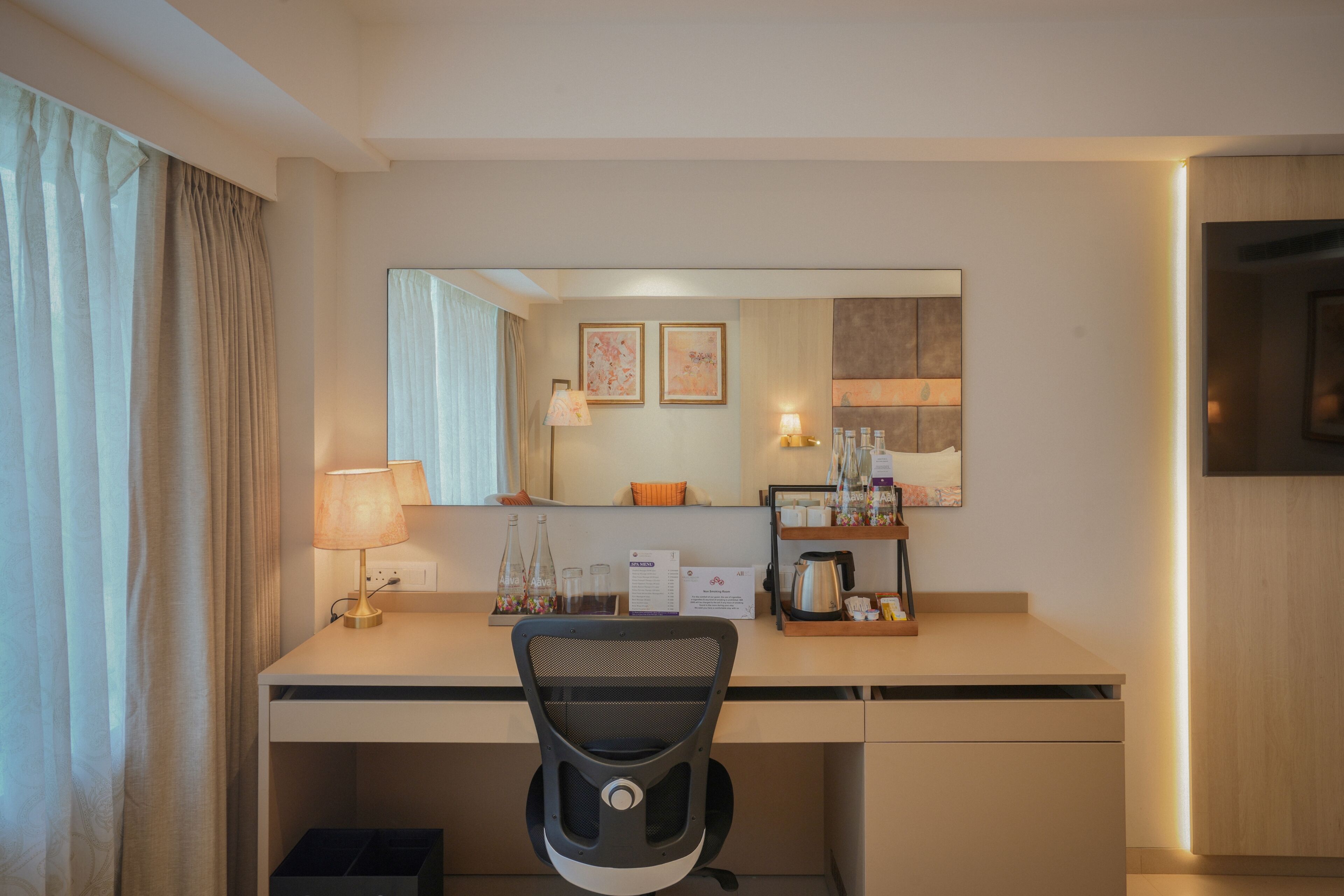 Habitación de hotel con escritorio, silla, lámpara, espejo y televisor.