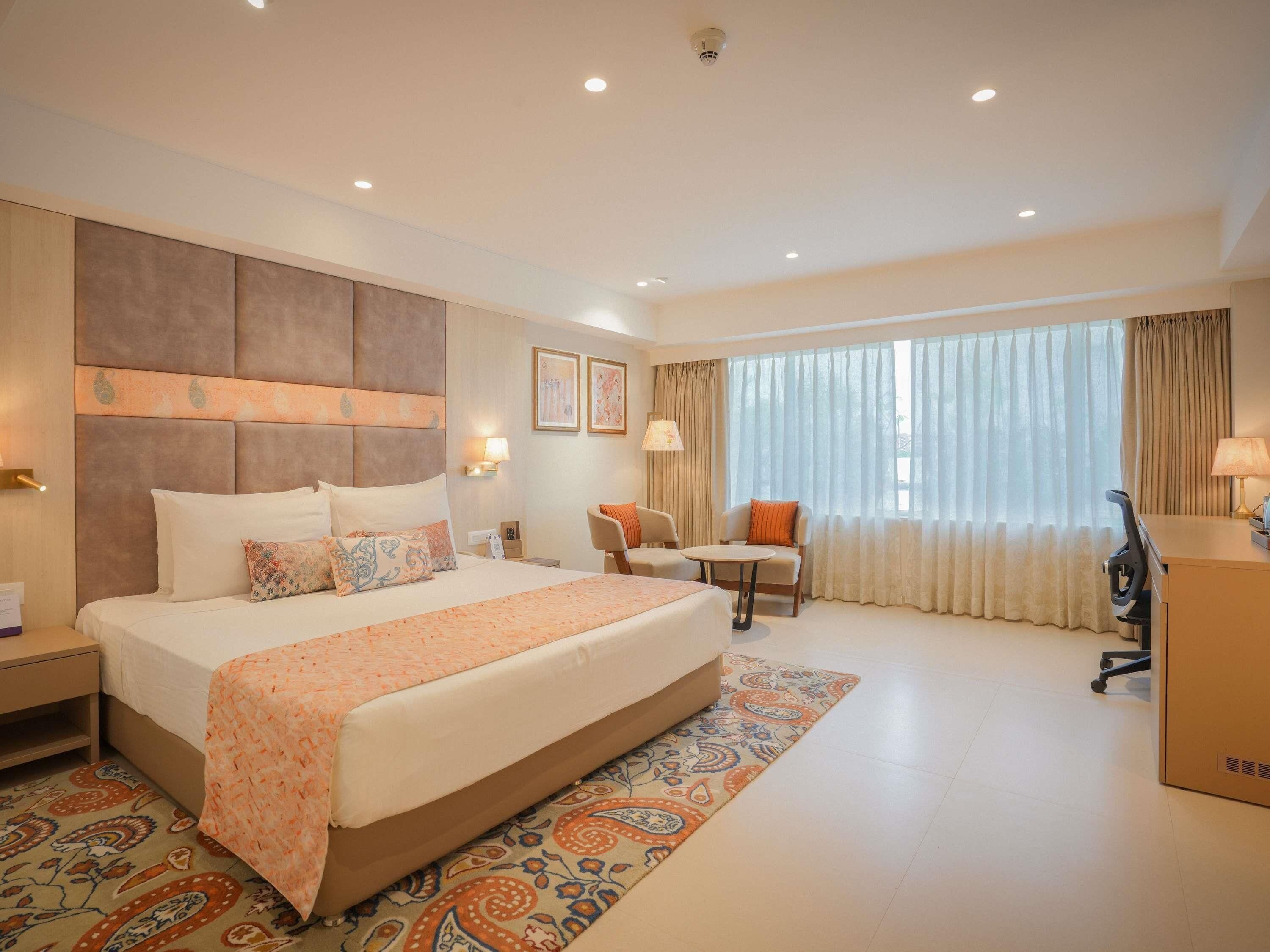 A hotel room with a large bed, a desk, a chair, and a window with curtains.