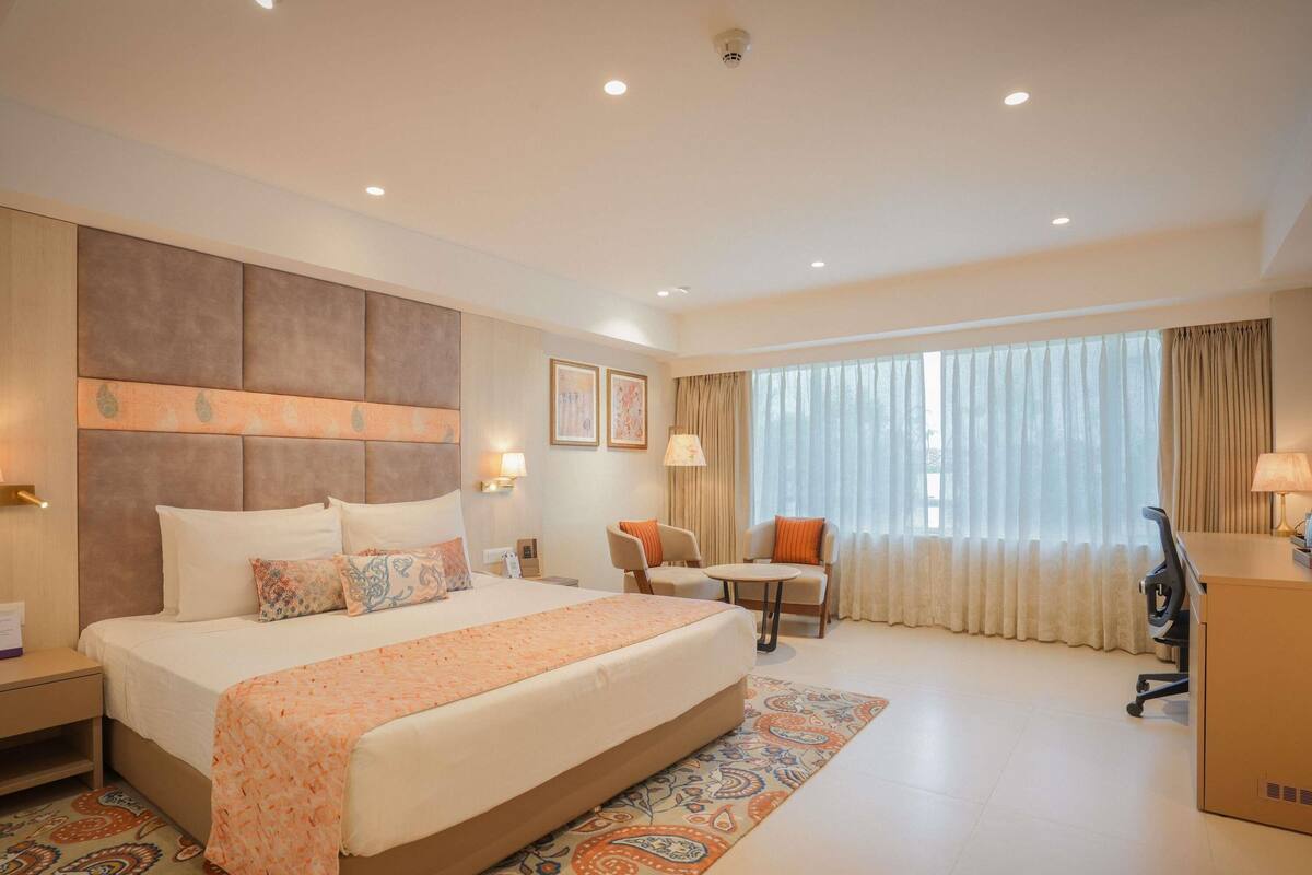 A hotel room with a large bed, a desk, a chair, and a window with curtains.