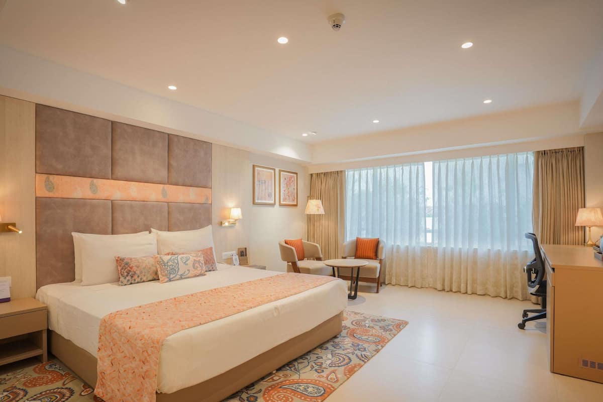 A hotel room with a large bed, a desk, a chair, and a window with curtains.