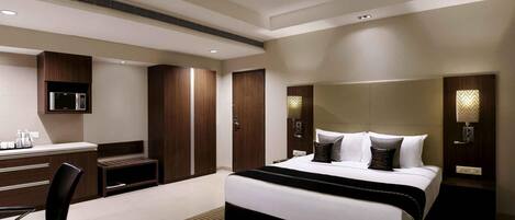 A modern hotel room with a bed, desk, chair, wardrobe, and wall-mounted lights.