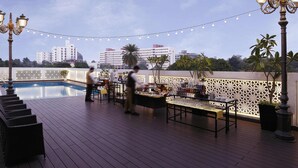 A rooftop pool area with a bar, outdoor seating, and string lights.