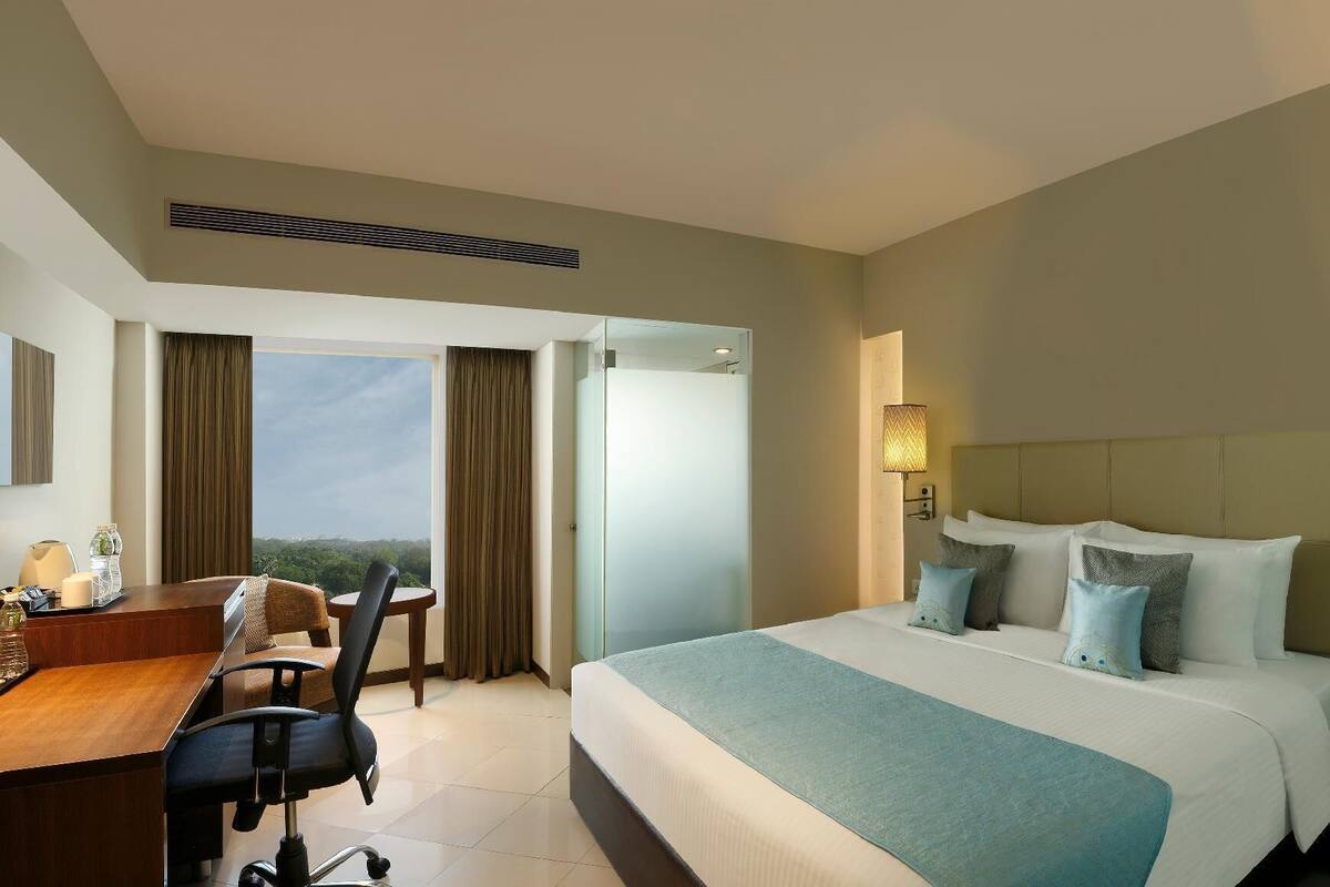 A hotel room with a bed, desk, chair, and a view of the outdoors.