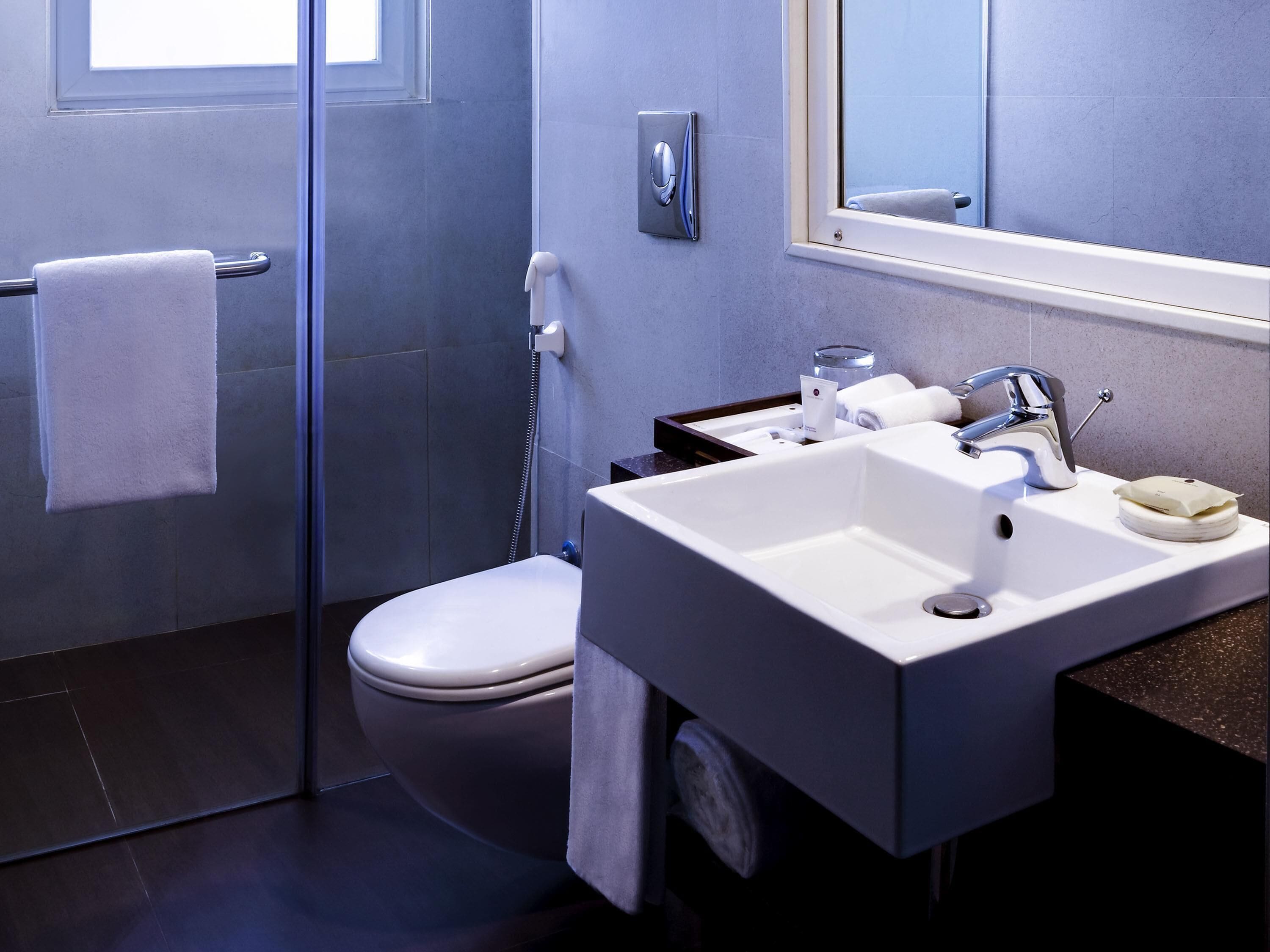 A modern bathroom with a glass shower enclosure, a toilet, a sink with a mirror, and a towel rack.