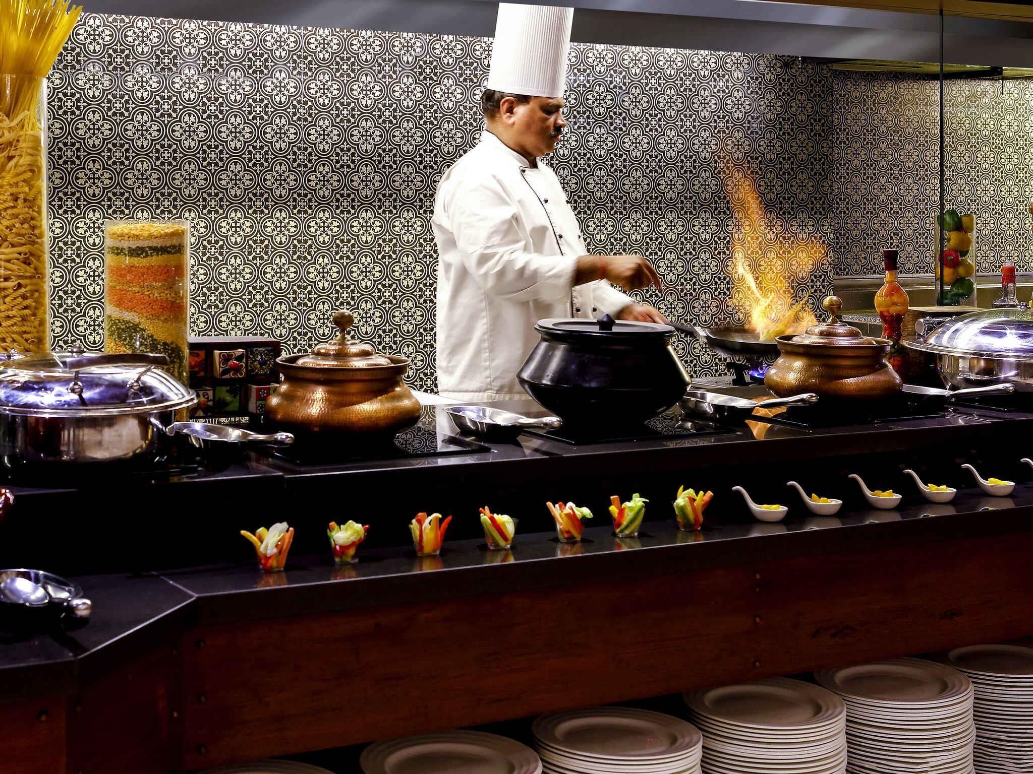 Un chef cocina en una cocina con baldosas estampadas, ollas y una variedad de alimentos sobre el mostrador.