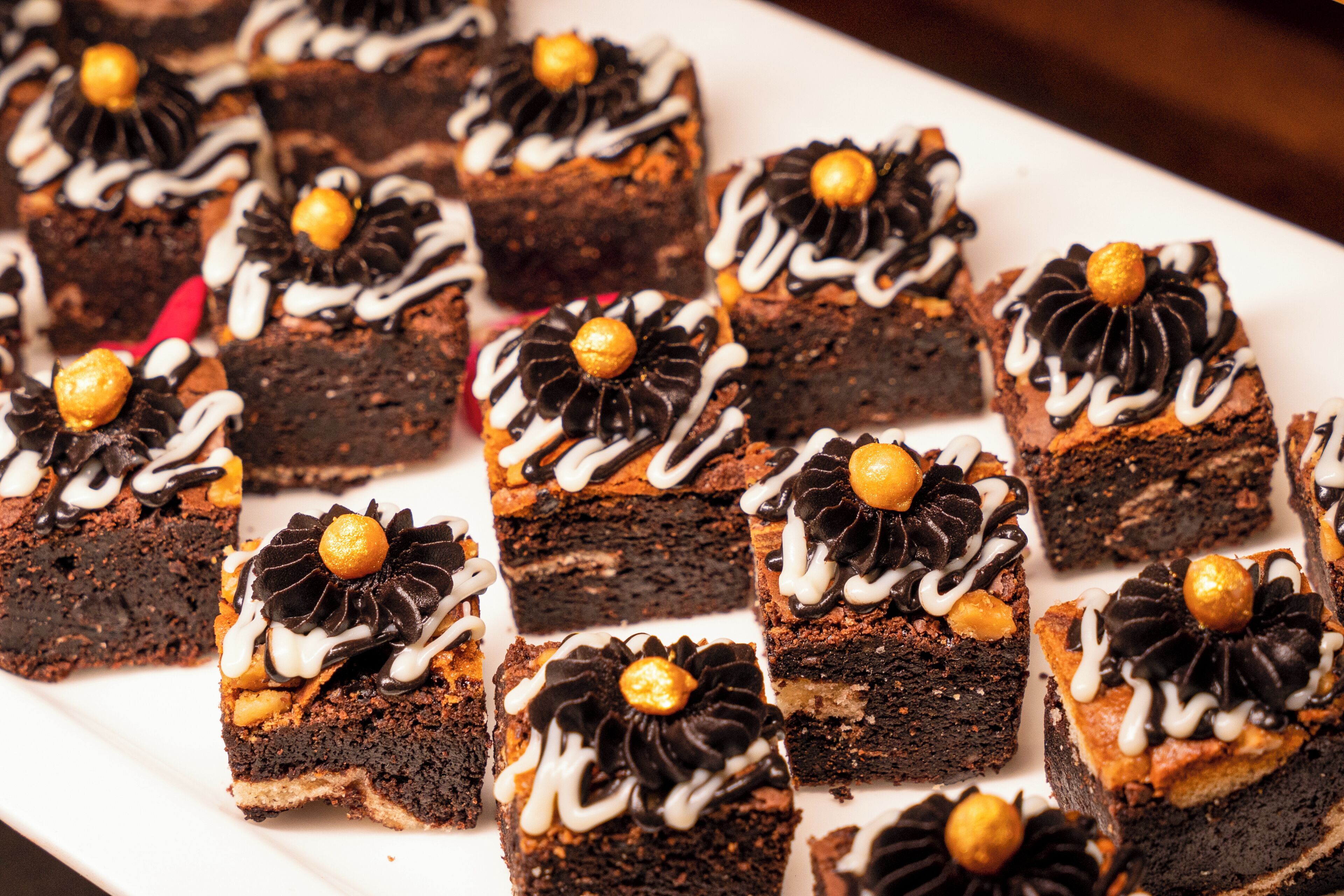 Um prato branco com vários brownies quadrados cobertos por glacê de chocolate e um fruto seco dourado.