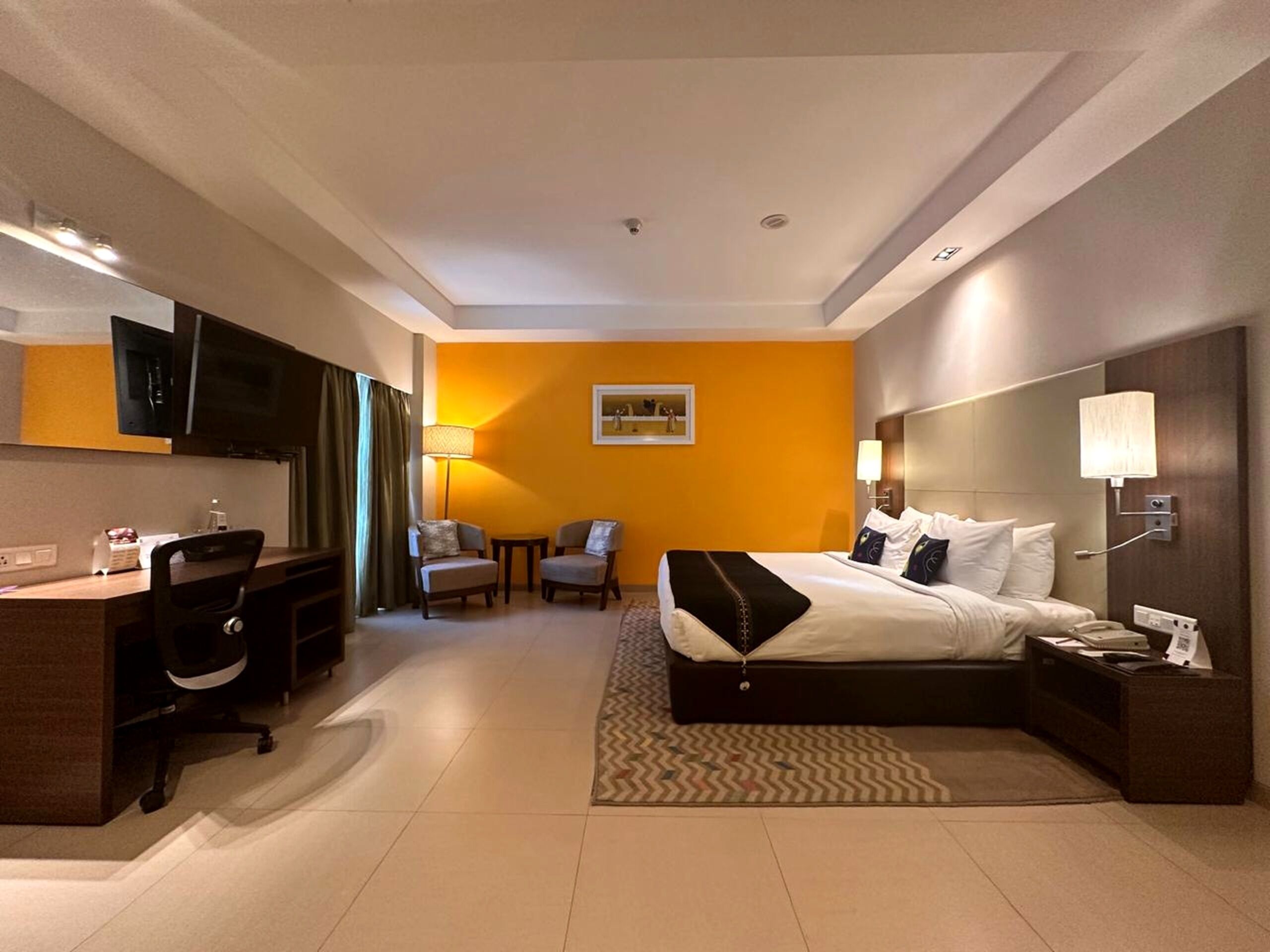Una habitación de hotel con cama, escritorio, sillas, televisor y lámpara.