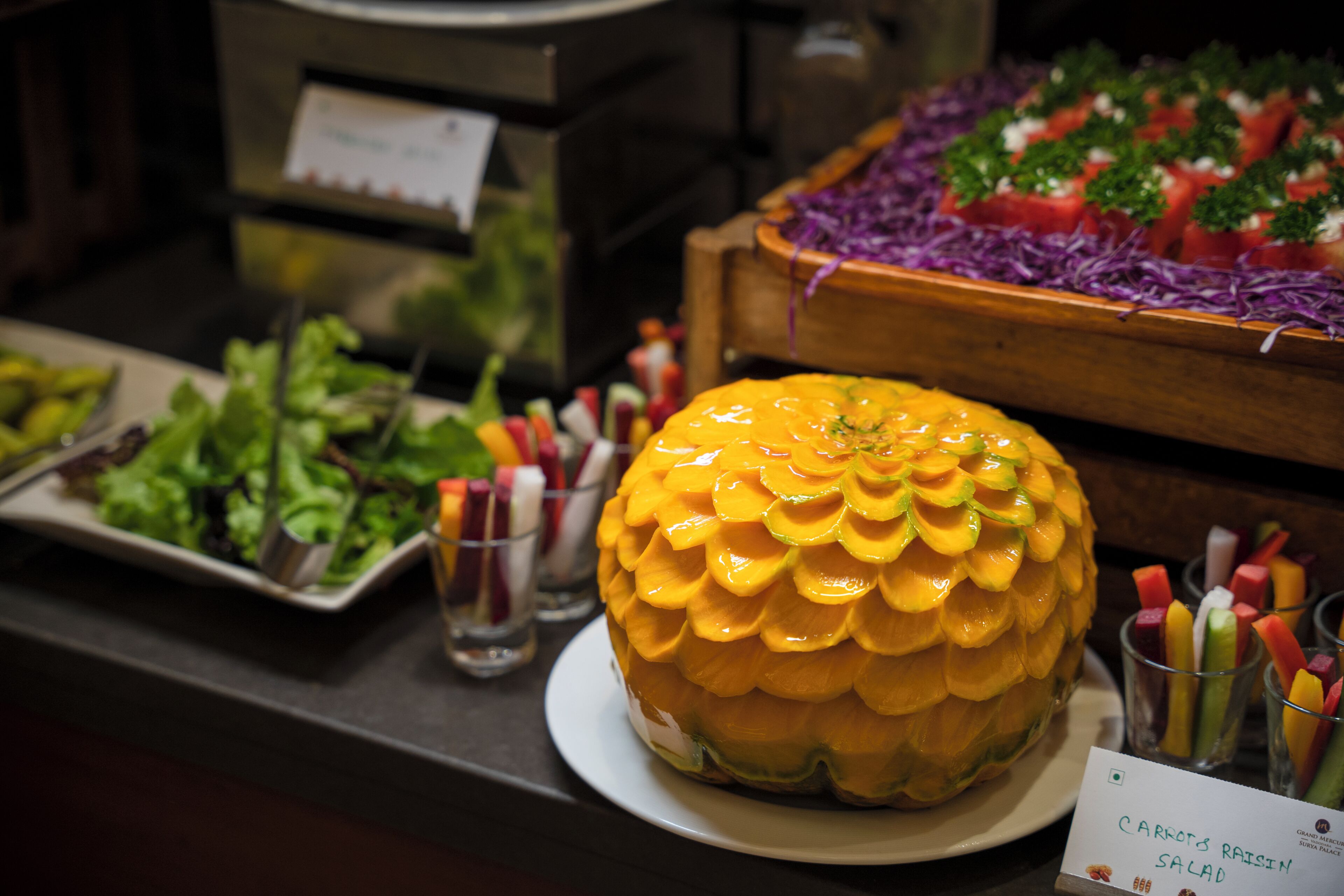 A fruit display with a carved pineapple centerpiece, a salad bar, and a sign for carrot salad.
