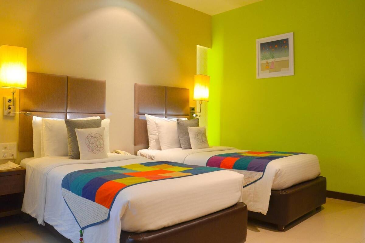 A hotel room with two beds, a green wall, and a painting.
