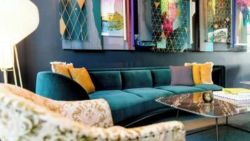 A modern living room with a teal sofa, patterned armchair, and a glass coffee table.