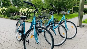 Una fila de bicicletas turquesas estacionadas sobre un área pavimentada, con un jardín y árboles al fondo.