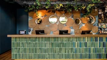 Un espace d’accueil doté d’un comptoir en bois, de trois miroirs ronds et d’un mur décoré de panneaux de bois circulaires et de plantes vertes.