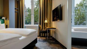 Habitación de hotel con cama, escritorio, silla, lámpara, televisor y vistas de la ciudad.