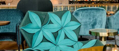 A bar area with teal upholstered chairs, a patterned rug, and a bar counter with bottles.