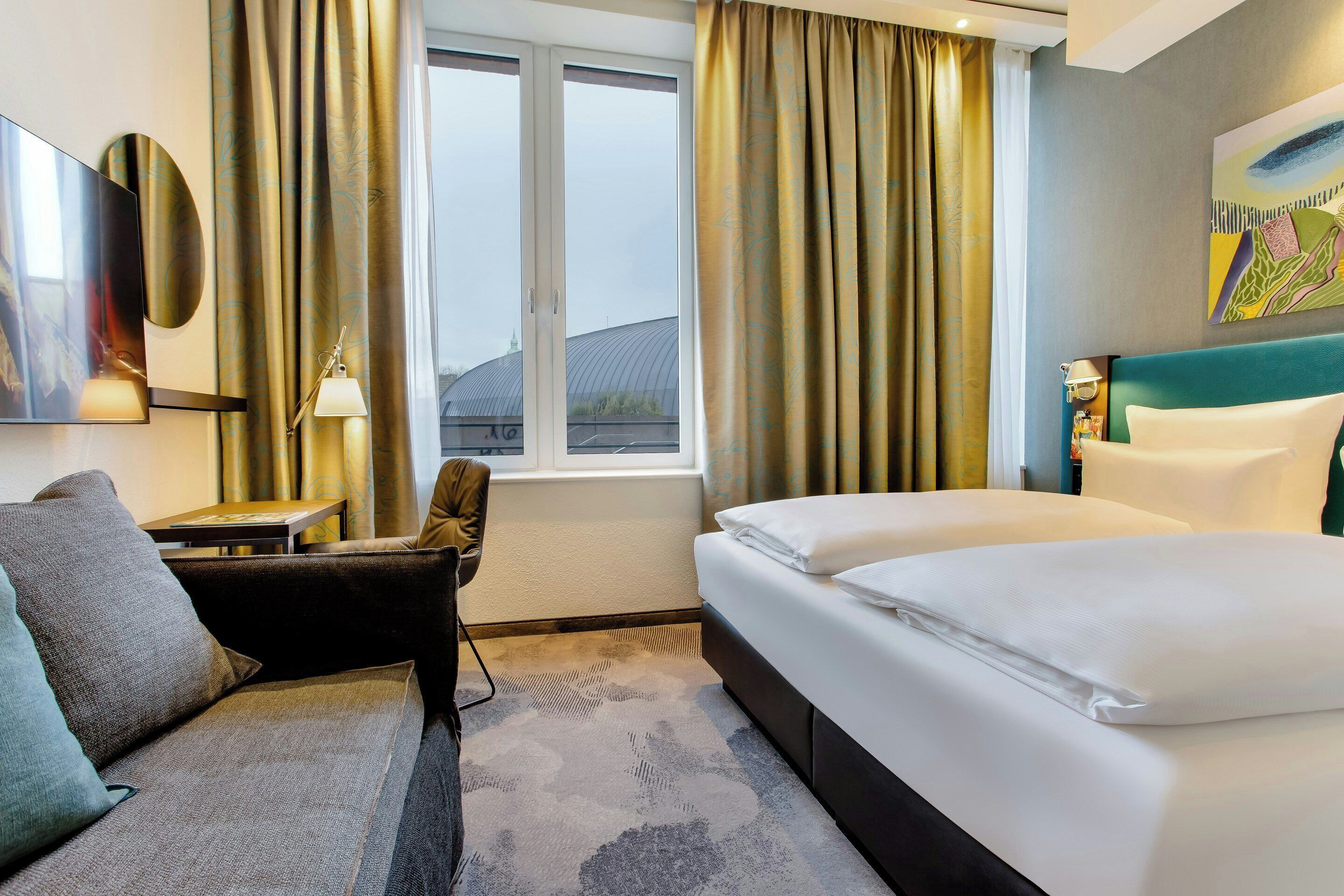 Ein Hotelzimmer mit Bett, Sofa, Schreibtisch und einem fenster mit Vorhängen.