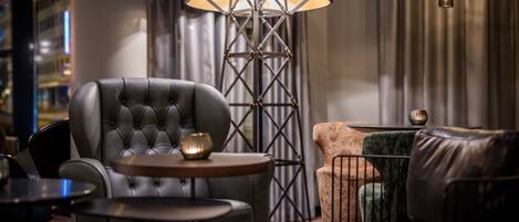 A modern lounge area with a tufted leather armchair, a round wooden table, and a floor lamp with a geometric base.