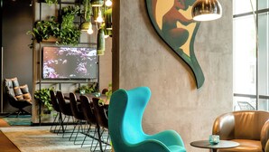 A modern lounge area with a teal chair, a brown leather sofa, and a TV screen displaying floral patterns.