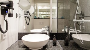 A modern bathroom with a large white sink, two round mirrors, a hairdryer, and a handheld showerhead.