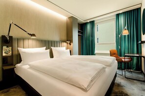 Habitación de hotel con dos camas, un escritorio, una silla y un amplio ventanal con cortinas.