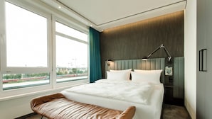 A modern hotel room with a large bed, a bench, a desk, and a view of a train outside the window.