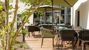 An outdoor seating area with wooden tables and chairs, large umbrellas, and a view of the building in the background.