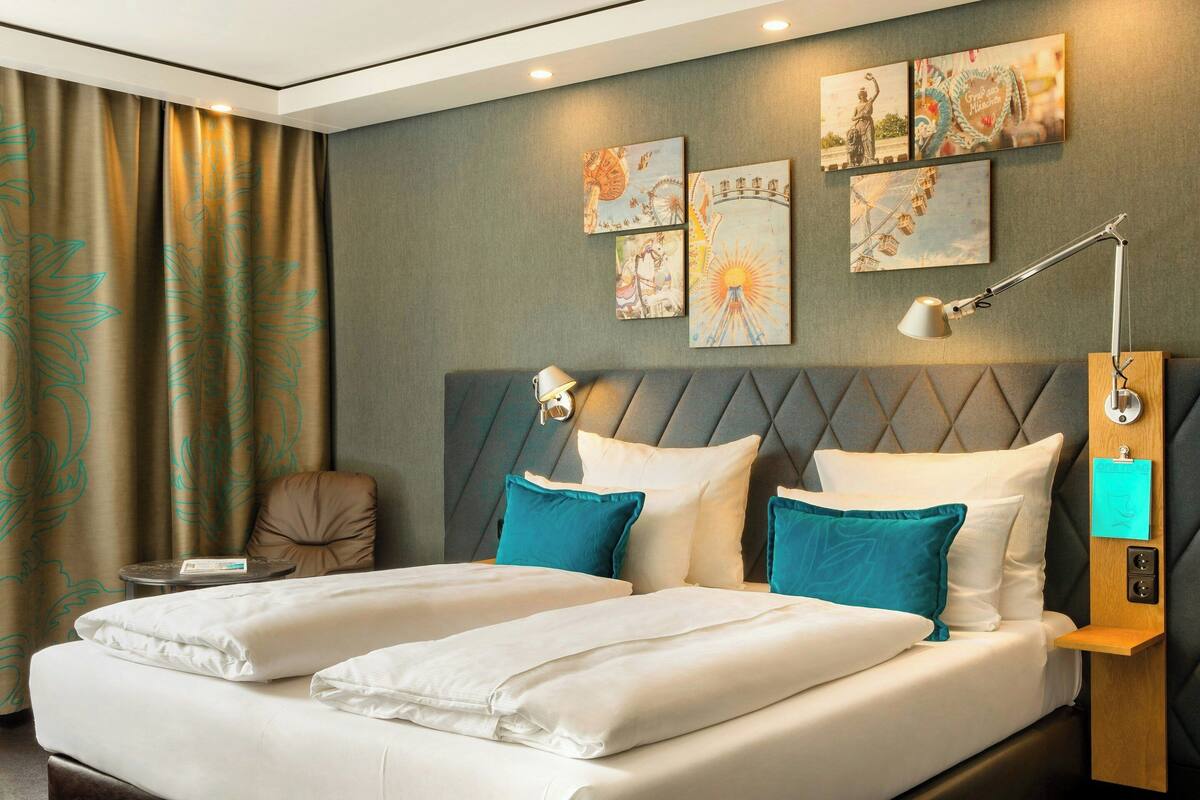 A hotel room with a double bed, two pillows, a bedside table, a lamp, and artwork on the wall.