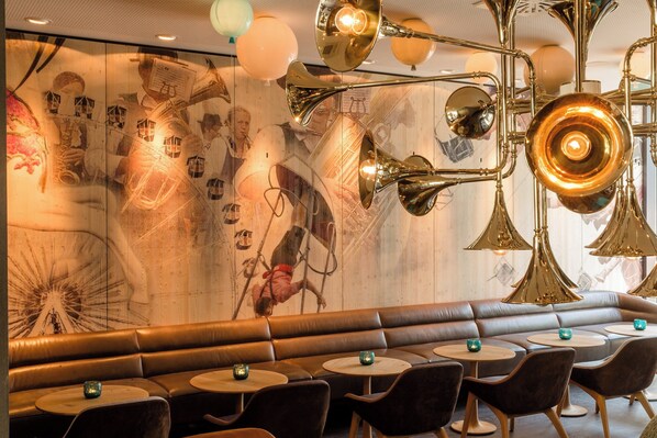 Un interior de restaurante con una larga banca de cuero marrón, mesas redondas y apliques de pared de latón.