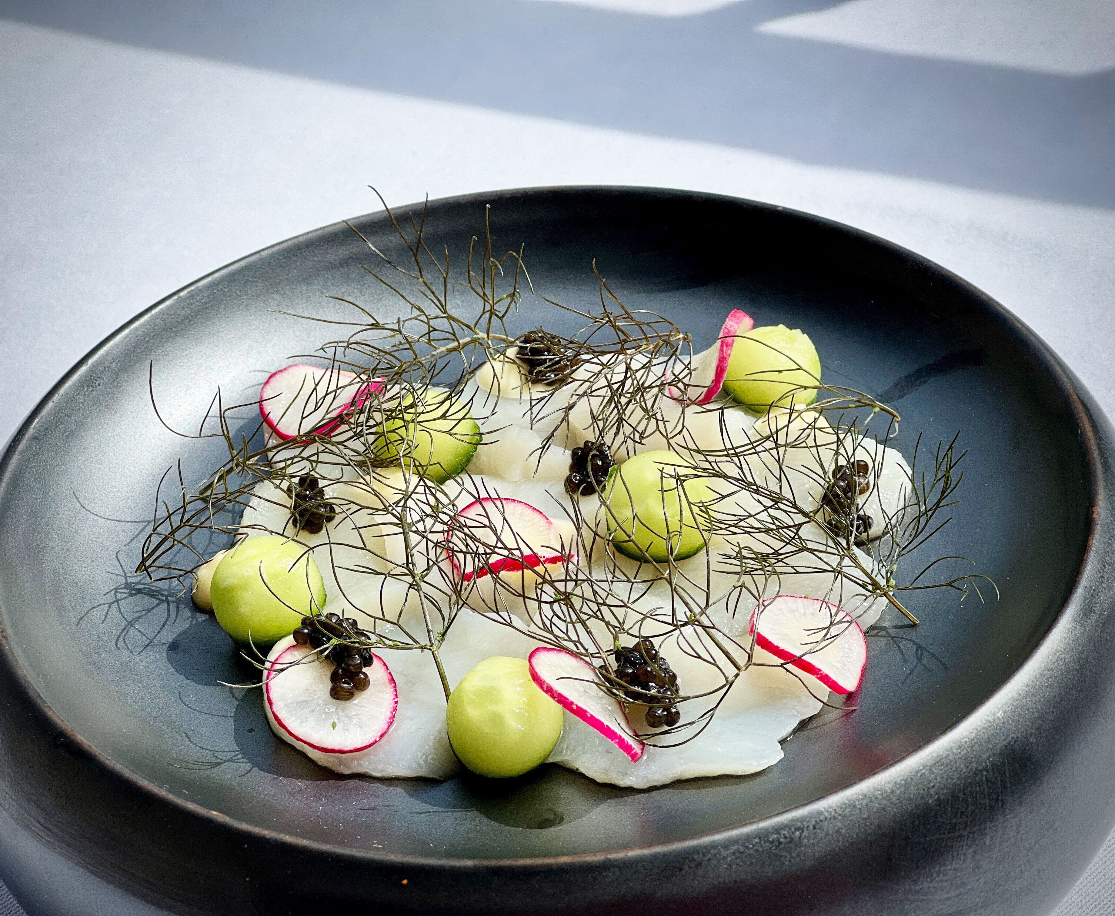Un plato con rábanos en rodajas, manzanas verdes y caviar negro, adornado con finas ramitas de eneldo.