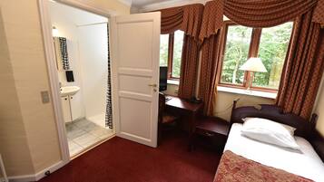 Une chambre d’hôtel comprenant un lit, un bureau, une chaise, une fenêtre avec des rideaux, une salle de bain avec un lavabo et un miroir.