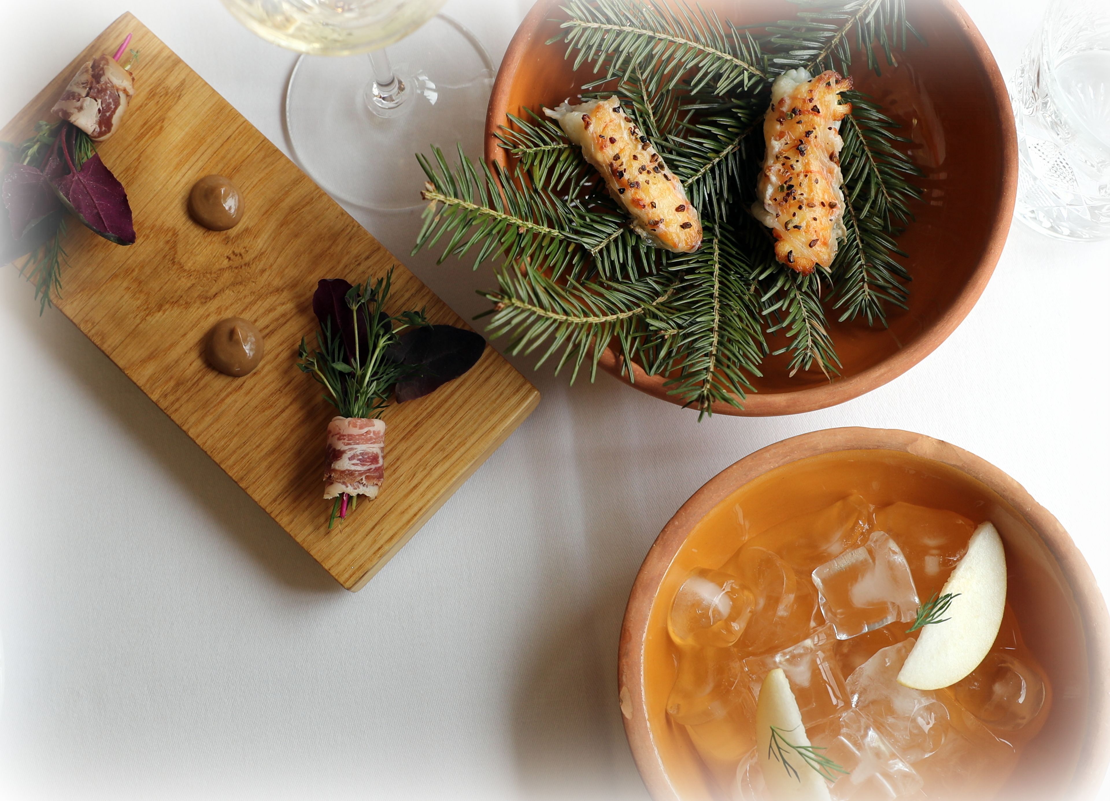 A wooden board with food items, a bowl of soup, and a glass of white wine on a table.